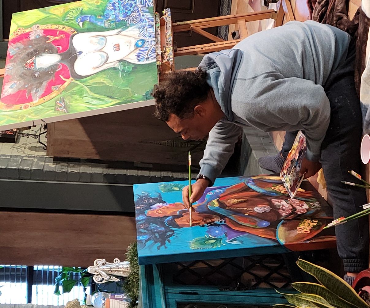 Bryant Benoit working on a canvas outdoors, more canvases around him