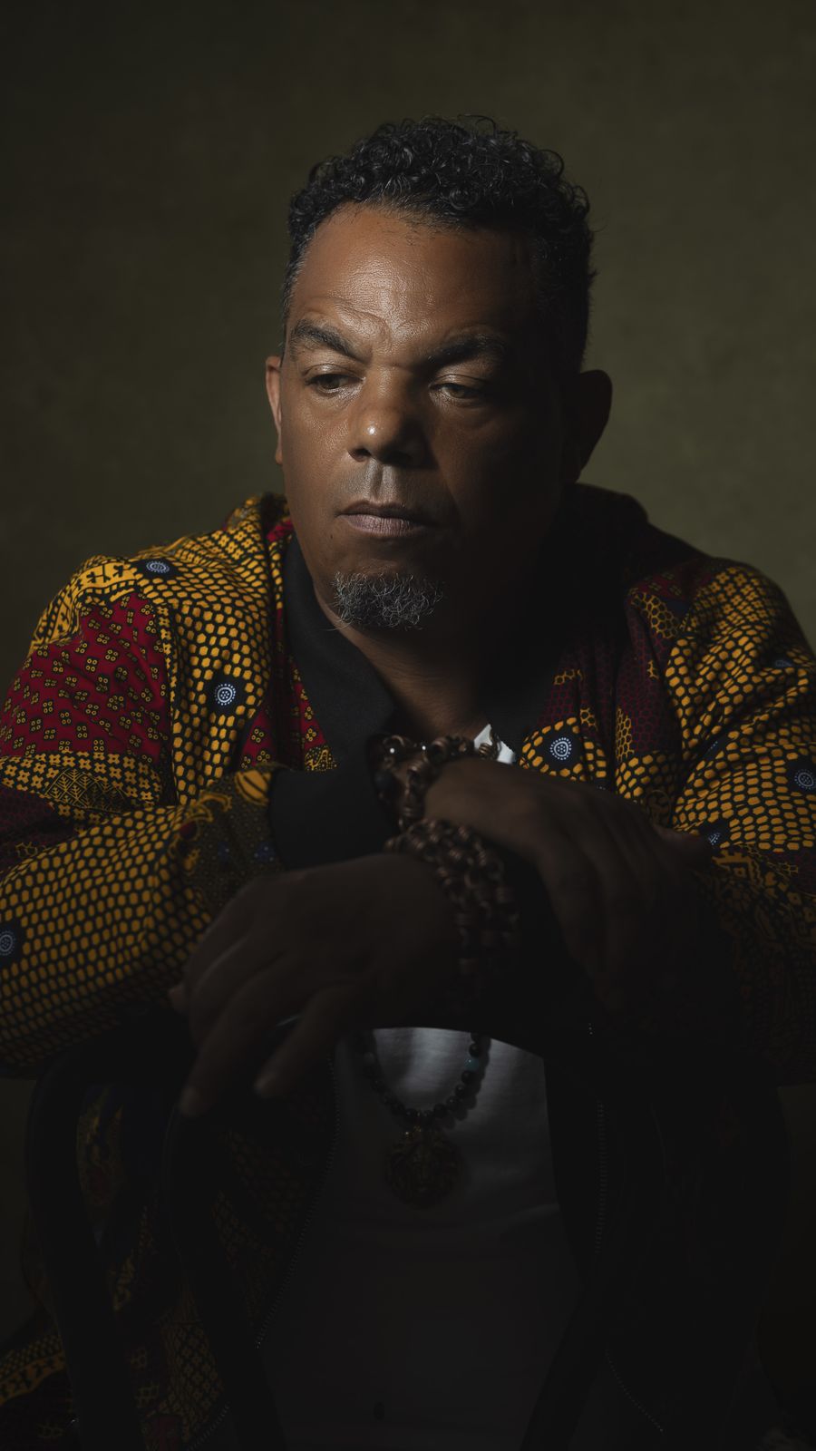 Bryant Benoit in a patterned jacket, seated in low studio light