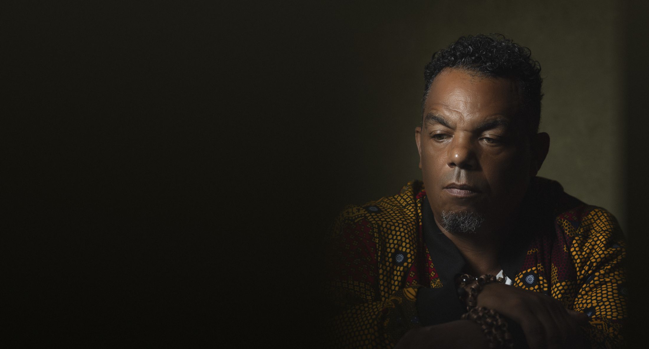 Portrait of Bryant Benoit in a patterned jacket, seated in low studio light